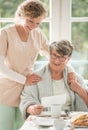 Senior lady on wheelchair with young volunteer in beige uniform supporting her