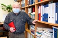 Senior male archivist holding red notebook and looking at camera, man wearing facial mask due coronavirus pandemic Royalty Free Stock Photo