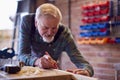 Senior Male Carpenter In Garage Workshop Measuring And Marking Piece Of Wood With Pencil Royalty Free Stock Photo