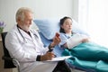 Senior male doctor checking brown medicine bottles of young patient woman in hospital bed Royalty Free Stock Photo