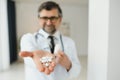 Senior male doctor with stethoscope in medical scrubs and holding bottle and tablets Royalty Free Stock Photo