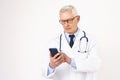 Senior male doctor text messaging on mobile phone while standing at isolated background Royalty Free Stock Photo