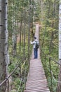 Senior male hiker taking pictures with cell phone on suspension bridge in forest. Nature park,Russia Royalty Free Stock Photo