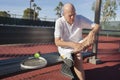 Senior male tennis player with leg pain sitting on bench at court Royalty Free Stock Photo