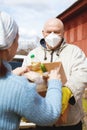 Senior male volunteer in mask gives an elderly woman boxes with food near her house Royalty Free Stock Photo