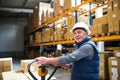 Senior male warehouse worker or a supervisor pulling a pallet truck with boxes. Royalty Free Stock Photo