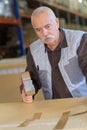 Senior male worker sealing cardboard box with in warehouse Royalty Free Stock Photo