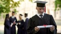 Senior man in academic regalia holding diploma, education at any age, new degree Royalty Free Stock Photo