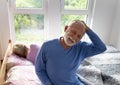 Senior man awakening and stretching neck in bed while woman still sleeping Royalty Free Stock Photo