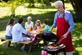 Senior man barbequing with family in background Royalty Free Stock Photo