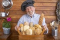 A senior man with beard and chef`s cap holds a basket with fresh bread made with different flours. Rustic background in recycled Royalty Free Stock Photo