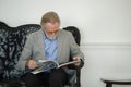 Senior man with beard and spectacles reading magazine sitting living room at home. elder male reading mag relaxation