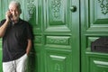 Senior man with beard and white hair standing and talking at mobile phone. Behind him a  large and green wooden door with the Royalty Free Stock Photo