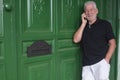 Senior man with beard and white hair standing and talking at mobile phone. Behind him a  large and green wooden door with the Royalty Free Stock Photo