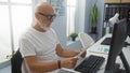 Senior man with beard working in a modern office, reviewing documents at his desk under natural light Royalty Free Stock Photo