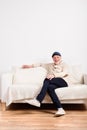 Senior man in beige sweater sitting on sofa, studio shot.