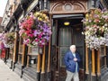 Senior man in blue jacket walks past entrance and floral baskets of Victorian style pub in city