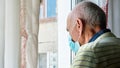 Senior man in blue sterile mask stands near window