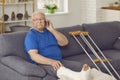 Senior man with broken leg sitting on couch at home and making call on smartphone Royalty Free Stock Photo