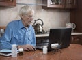 Senior man browsing laptop computer making online payment sitting in kitchen. Buying drugs online Royalty Free Stock Photo