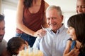 Senior man celebrating his birthday with family after blowing out candles on birthday cake, close up