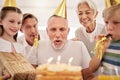 Senior man celebrating his birthday with his family at home, wearing party hats and blowing whistles. Grandpa blowing Royalty Free Stock Photo