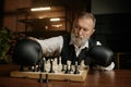 Senior man chess player moving chesspiece on board while wearing in boxer gloves
