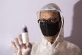 Senior man with corona preventive mask and PPE suit showing ampul in front of a white copy space background. Royalty Free Stock Photo