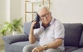 Senior man with dementia sitting on the sofa and holding a shoe like a telephone