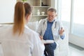 Senior man doctor examining yound woman in doctor office or at home. Girl patient and doctor have consultation in Royalty Free Stock Photo