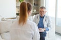 Senior man doctor examining yound woman in doctor office or at home. Girl patient and doctor have consultation in Royalty Free Stock Photo