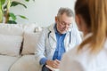 Senior man doctor examining yound woman in doctor office or at home. Girl patient and doctor have consultation in Royalty Free Stock Photo