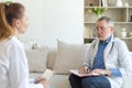 Senior man doctor examining yound woman in doctor office or at home. Girl patient and doctor have consultation in Royalty Free Stock Photo