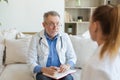 Senior man doctor examining yound woman in doctor office or at home. Girl patient and doctor have consultation in Royalty Free Stock Photo