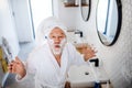 A senior man doing morning routine in bathroom indoors at home.