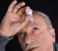 Senior man dripping a red bloodshot eye with eye drops Royalty Free Stock Photo