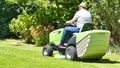 Senior man driving a tractor lawn mower in garden with flowers