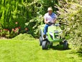Senior man driving a tractor lawn mower in garden with flowers Royalty Free Stock Photo