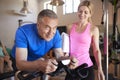 Senior Man Exercising On Cycling Machine Being Encouraged By Female Personal Trainer In Gym Royalty Free Stock Photo