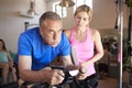 Senior Man Exercising On Cycling Machine Being Encouraged By Female Personal Trainer In Gym Royalty Free Stock Photo