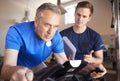 Senior Man Exercising On Cycling Machine Being Encouraged By Personal Trainer In Gym Royalty Free Stock Photo