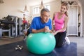 Senior Man Exercising On Swiss Ball Being Encouraged By Personal Trainer In Gym Royalty Free Stock Photo