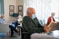 Senior man with face mask reading book at assisted living centre Royalty Free Stock Photo