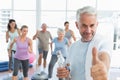 Senior man gesturing thumbs up with people exercising in fitness studio Royalty Free Stock Photo