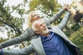 Mature man giving woman piggyback ride through park Royalty Free Stock Photo