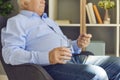 Senior man with glass of water taking prescribed pills sitting in an armchair at home Royalty Free Stock Photo