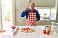 Senior man with grey hair cooking pizza at home kitchen pointing finger up with successful idea Royalty Free Stock Photo