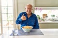 Senior man with grey hair eating pasta spaghetti at home doing happy thumbs up gesture with hand Royalty Free Stock Photo