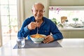 Senior man with grey hair eating pasta spaghetti at home with a happy and cool smile on face Royalty Free Stock Photo