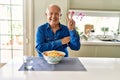 Senior man with grey hair eating pasta spaghetti at home smiling with happy face winking at the camera doing victory sign Royalty Free Stock Photo